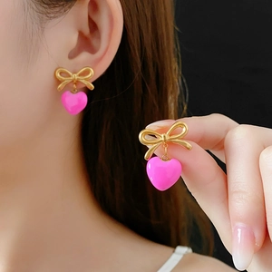 Détail des boucles d'oreilles nœud doré avec pendentifs cœur rose sur le mannequin
