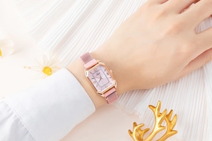 Detail of rose gold rectangular watch with pink mesh band on a model's wrist