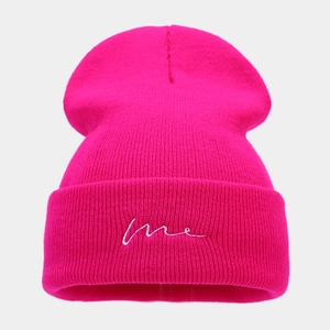 Detail of rose red knitted beanie with white 'me' embroidery on the ribbed cuff