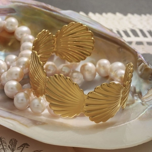 Golden titanium steel wide bracelet with shell design in a marine setting with pearls