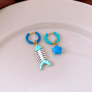 Detailed shot of asymmetric fishbone and star drop earrings with blue enamel finish