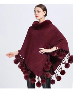 Close-up of wine red knit poncho featuring faux fur collar and decorative pom-pom tassels
