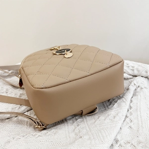 Detail of quilted beige PU leather backpack with cat charm and precise stitching