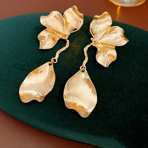 Detailed view of gold petal earrings with floral texture on dark green velvet padding