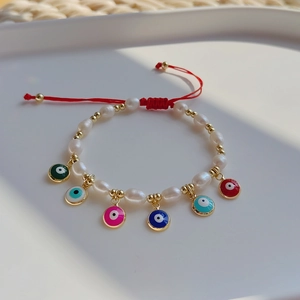 Detail of beaded evil eye charms on baroque pearls bracelet with red woven cord