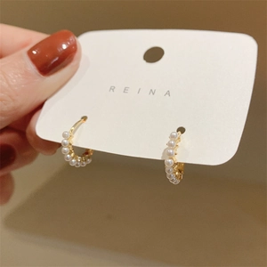 Macro detail of gold hoop earrings with small white pearls on a display card