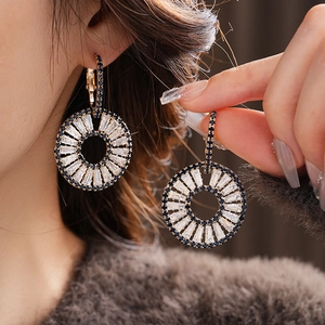 Detail of gold-tone geometric hoop earrings with blue and white zircon stones on model
