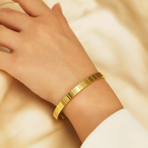 Dettaglio di un bracciale dorato con motivo a scacchi indossato su uno sfondo di seta