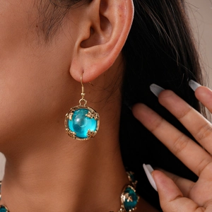 Détail de boucles d'oreilles rétro dorées avec résine bleue et motifs floraux ciselés