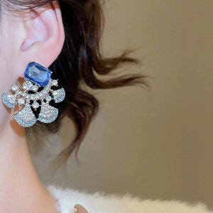 Close-up of elegant fan-shaped earrings with blue crystals worn by a model