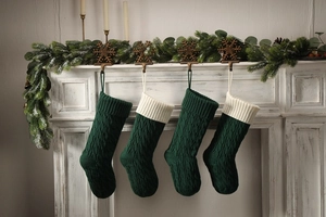 Close-up of four dark green knitted Christmas stockings with cream white cuffs on fireplace