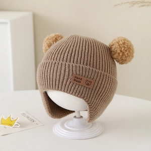 Detailed knit texture and handmade bear label on warm winter baby hat with pom-poms