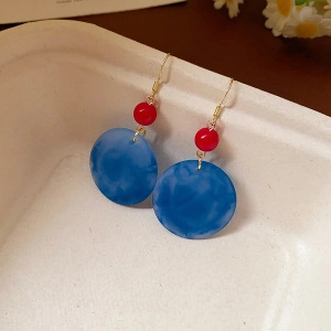 Detail view of red round beads and blue marble acrylic tassel earrings on a tray