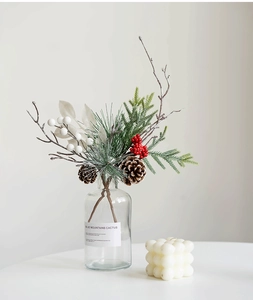 Close-up of Christmas arrangement with red berries, pine cones, and clear glass vase