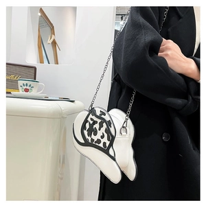 Detail view of heart-shaped handbag with cow print flap and silver chain strap on model
