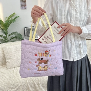 Close-up of quilted purple tote bag with dog embroidery and yellow handles on sofa
