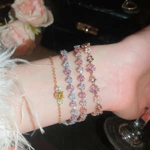 Close-up of stacked gold floral bracelets with pink and yellow cubic zirconia stones