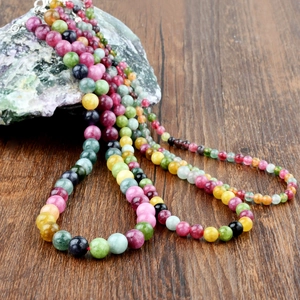 Vintage multi-color tourmaline beaded necklace displayed on dark wood and raw stone