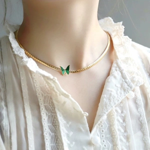 Detail of flat gold snake chain with green enamel butterfly pendant on model neck