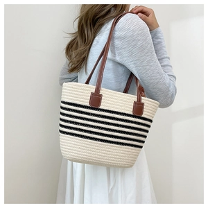 Dettaglio di una borsa tote in paglia a righe con spalline in pelle marrone su modella