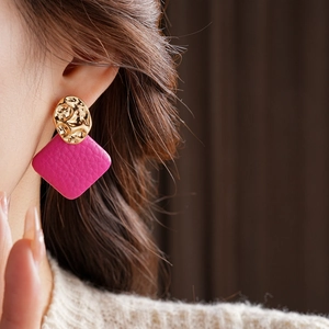 Close-up of rose red leather and gold hammered metal irregular stud earrings on model