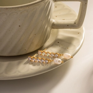 Detailed view of long gold tassel earrings featuring zircon stones and white pearls