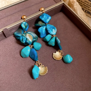 Detailed shot of long beach style earrings with blue shell beads and golden pendants