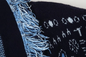 Macro shot of the detailed knit jacquard pattern and fringe trim on the navy blue cardigan