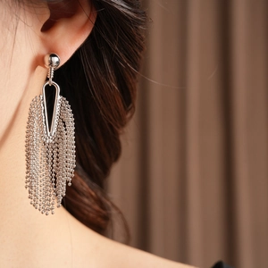 Detail view of silver tassel earrings with metallic bead chains worn by a model