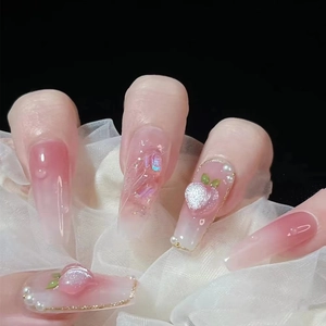 Close-up of pink gradient press-on nails with 3D peach charms and pearl accents
