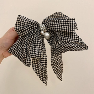 Detail of houndstooth bow hair clip featuring elegant white pearl center and pendant
