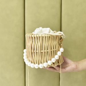 Close-up of handwoven straw bucket bag featuring a pearl handle and gold chain strap