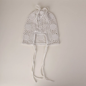 Détail de la maille crochetée blanche à motifs ajourés sur un bonnet bohème à lanières
