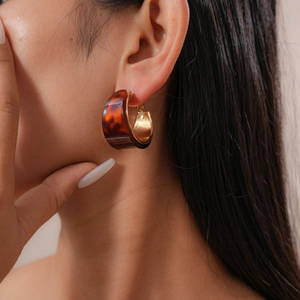 Close-up of retro brown tortoise resin C-shaped earrings with a golden metal inner layer