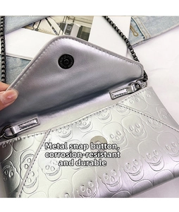Detail of silver skull embossed handbag featuring a magnetic snap closure and metal chain