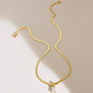 Golden snake chain necklace with rectangular zircon pendant on warm beige background