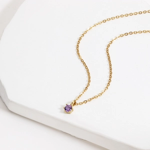 Close-up of 18K gold-plated chain with a round purple zircon pendant on a stone surface