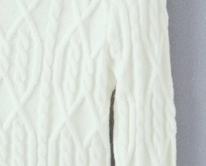 Detailed close-up of white cable knit pattern on a slim-fit knit sweater and skirt set