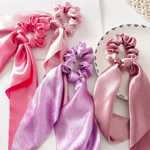 Flat lay of four satin ribbon scrunchies in pink and purple shades for hair styling