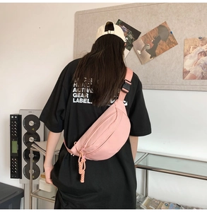 Outdoor view of a light pink nylon crossbody bag showing the back strap and buckle