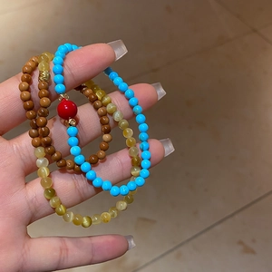 Détail de bracelets superposés en turquoise, bois et œil de chat portés au poignet