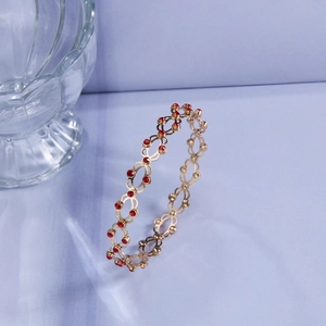 Detail eines goldenen Armbands im Vintage-Stil mit roten Strasssteinen und filigranem Muster