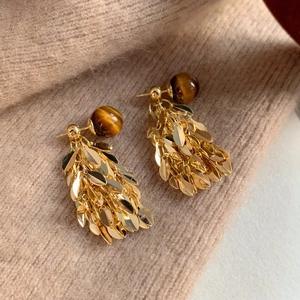 Golden leaf tassel earrings with tiger eye beads on beige knit fabric background