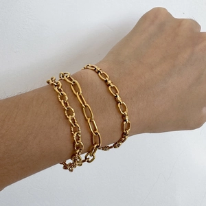 Ensemble de trois bracelets chaîne dorés de luxe portés au poignet sur un fond blanc pur