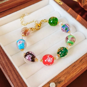 Close-up of glass beads with floral patterns and gold leaf on a wooden jewelry box