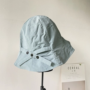 Detail of light green bucket hat with side criss-cross straps and black buttons decoration