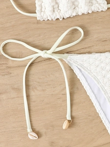 Detailed close-up of white textured bikini bottoms featuring side ties and shell charms