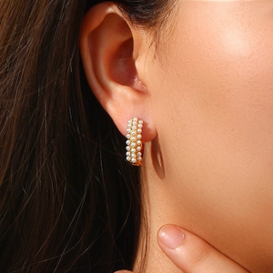 Close-up of 18K gold plated hoop earrings with triple rows of white pearls on a model