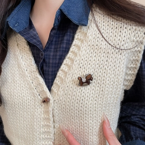 Detail of a vintage-style flocked resin horse brooch on a beige knit sweater vest