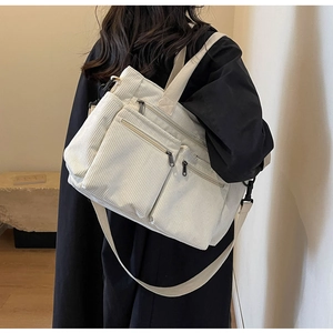 Detail of white corduroy tote bag showing multiple zipper pockets and adjustable strap